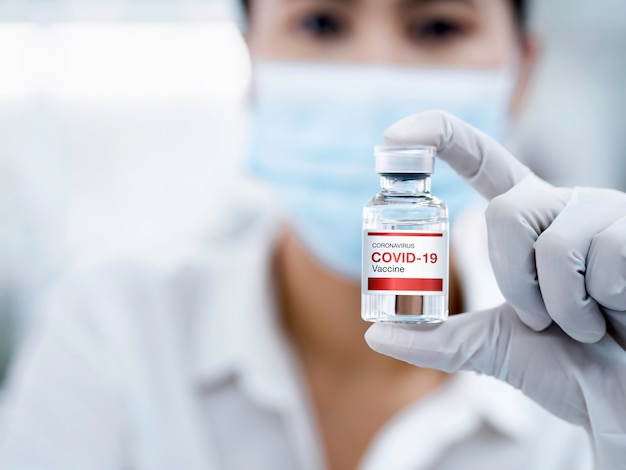 Schließen Sie den modernen Covid19-Impfstoff auf der Flaschendurchstechflasche, die von einer Ärztin mit Gummihandschuhen im Labor gezeigt wird