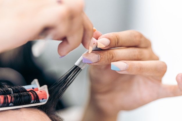 Schließen Sie den selektiven Fokus auf die lackierten Nägel eines Friseurs, während Sie das Haar eines Kunden kräuseln