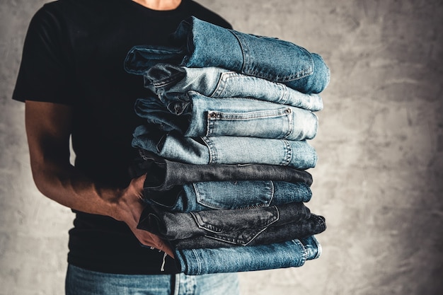 Schließen Sie den Stapel gefalteter Jeans in der Hand über grauem Wandhintergrund, Kopienraum