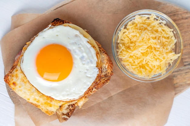 Schließen Sie die Draufsicht auf das heiße Sandwich French Croque Madame, das mit Käse überbacken und mit Spiegelei auf Papier gekrönt ist