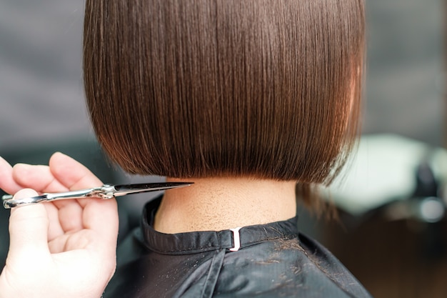 Schließen Sie die Hände eines professionellen Friseurs, der die Haare mit einer Schere schneidet