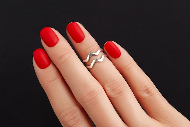 Schließen Sie die Hand der Frau mit roten matten Nägeln auf schwarzem Hintergrund Maniküre-Pediküre-Designtrends