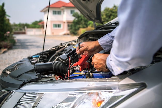 Schließen sie die hand des automechanikers mit der messung der autobatterie.