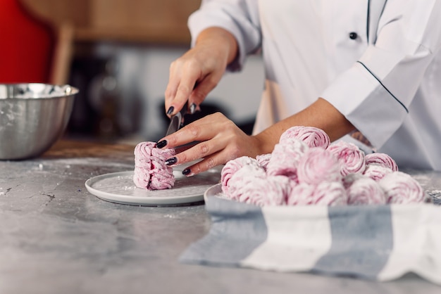 Schließen Sie die Hand des Küchenchefs, die frisch gemachte Marshmallows mit einem Messer schneidet. Überprüfung der Qualität von hausgemachtem Marshmallow.