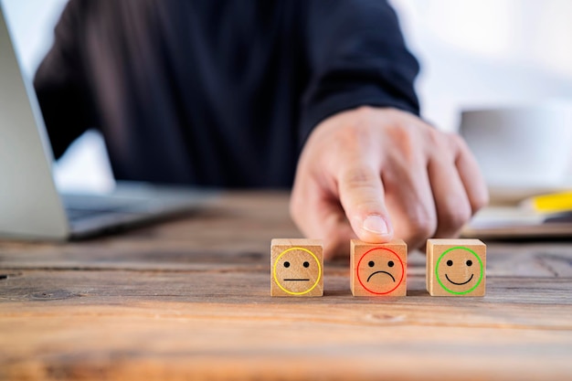 Schließen Sie die Hand des Kunden, wählen Sie ein trauriges Gesicht und ein Smiley-Gesichtssymbol auf einem Holzwürfel Service-Rating-Zufriedenheitskonzept