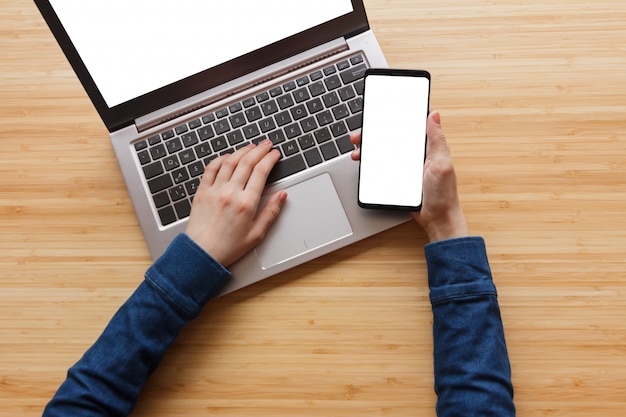 Schließen Sie die Hand mit dem weißen Bildschirm des Telefons und des Laptops auf dem Arbeitsbereichstisch.