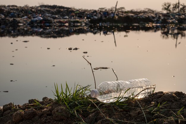 Schließen sie einen klaren plastikflaschentropfen auf dem boden mit verschmutztem wasser und großem bergmüll im hintergrund