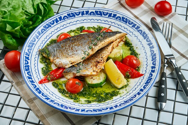 Schließen Sie herauf Ansicht auf frischem gebratenem Seebarsch, der mit Kartoffel und Tomatenkirsche in der weißen Platte serviert wird. Lebensmittelfoto für Menü oder Rezept. Selektiver Fokus. Gesunde Meeresfrüchte zum Mittagessen Wolfsbarsch