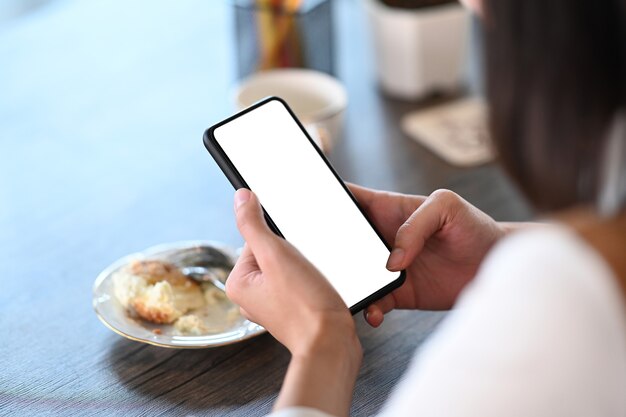 Schließen Sie herauf Ansicht der jungen Frau, die im Café sitzt und Smartphone mit weißem Bildschirm hält.