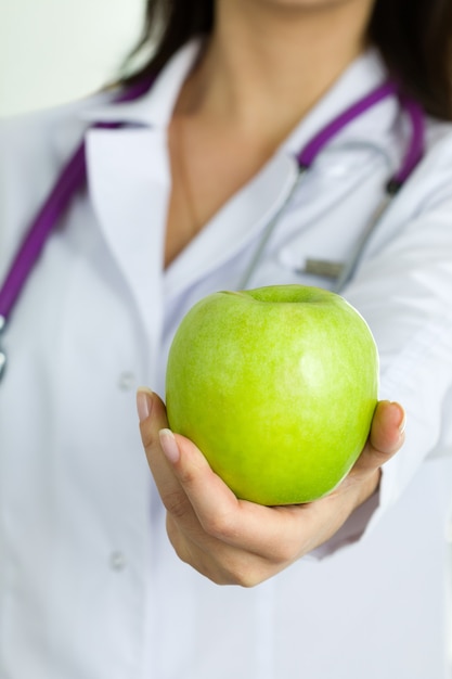 Schließen Sie herauf Ansicht der weiblichen Arzthand, die grünen Apfel anbietet. Gesundes Essen und Lebensstil, Gesundheitswesen, medizinischer Service und Diät-Esskonzept