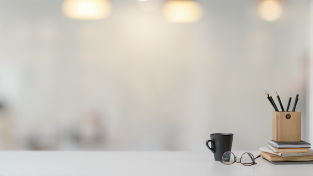 Schließen Sie herauf Ansicht des Arbeitsbereichs mit Briefpapier, Gläsern und Kaffeetasse auf weißem Tisch mit unscharfem Hintergrund