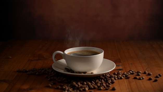 Schließen Sie herauf Ansicht einer Tasse heißen Kaffees mit Kaffeebohnen, die auf Holztisch verziert werden