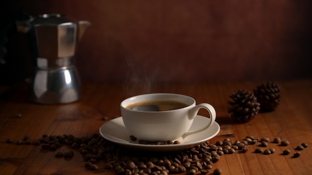 Schließen Sie herauf Ansicht einer Tasse Kaffee und Kaffeekanne auf Holztisch verziert mit Kaffeebohnen