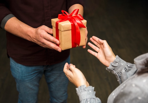 Schließen Sie herauf Ansicht von Händen eines Mannes, der einer Frau ein Geschenkpaket mit einem Bogen übergibt