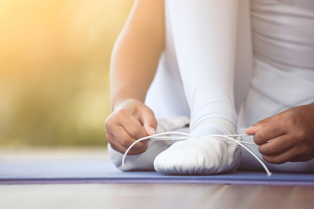 Schließen Sie herauf das asiatische Kindermädchen, das auf den Füßen pointe Schuhen bindet, die für das Üben eines Balletts sich vorbereiten