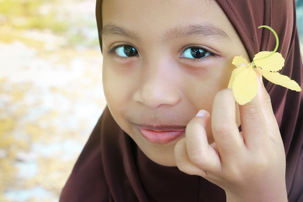 Schließen Sie herauf das entzückende moslemische Mädchengesicht, das hijab trägt, gelbe Blume lächelt und hält.