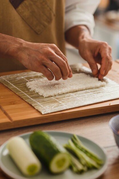 Schließen Sie herauf, das männliche Sushi-Hände macht, die Reis für das Rollen auf einer asiatischen Lebensmittellieferung der Bambusmatte vorbereiten