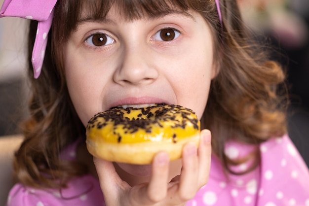 Schließen Sie herauf das Schulmädchen, das Donut isst, während es zu Hause am Tisch sitzt Porträt eines Mädchens, das Donut wählt