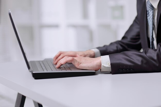 Schließen Sie herauf den Geschäftsmann, der auf Laptop schreibt, während er am Tisch sitzt