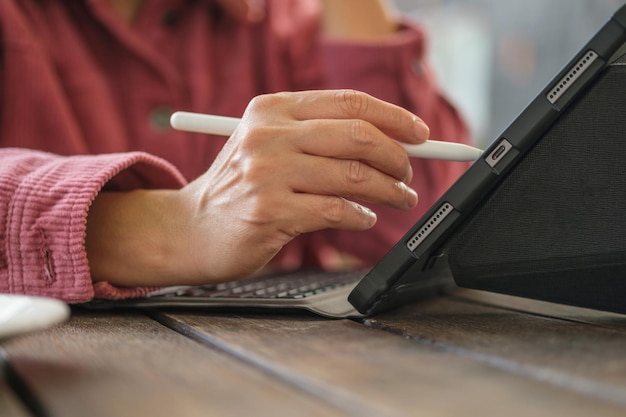 Schließen Sie herauf den Handgebrauchsstift der Frau, der mit Tablet online im Café arbeitet