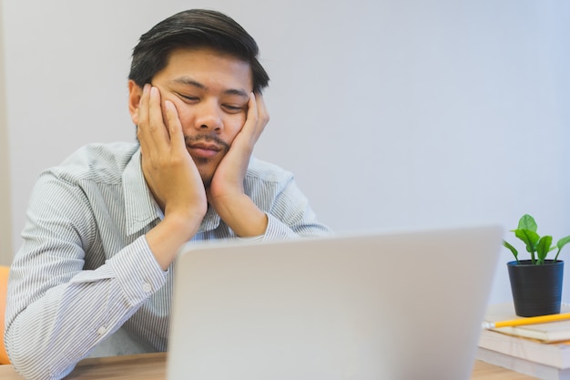 Schließen Sie herauf den jungen asiatischen Mann, der am Schreibtisch, Lebensstilkonzept gelangweilt und schläfrig sich fühlt