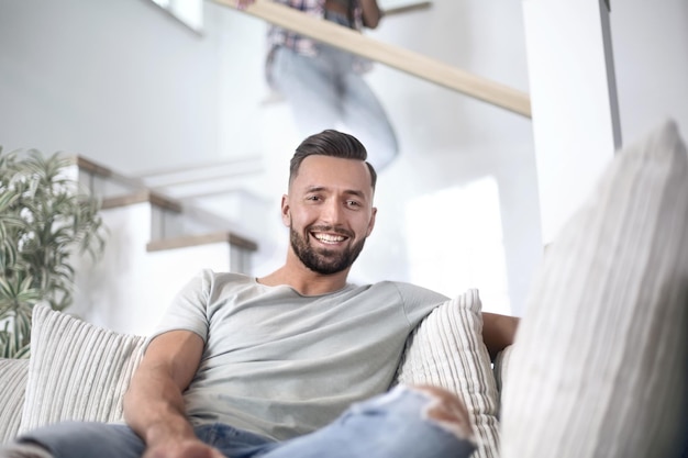 Schließen Sie herauf den jungen Mann, der auf Sofa sitzt