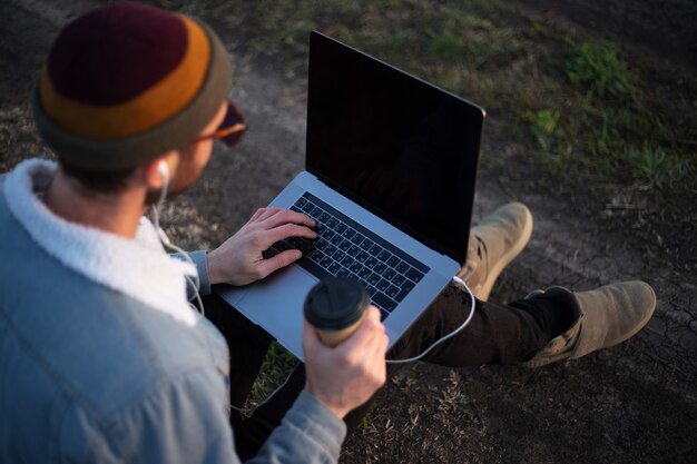 Schließen Sie herauf des jungen Mannes, der mit Laptop auf Beinen und Tasse Kaffee in der Hand sitzt