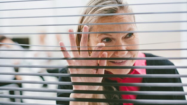 Schließen Sie herauf die erwachsene Geschäftsfrau, die vor dem Bürofenster steht