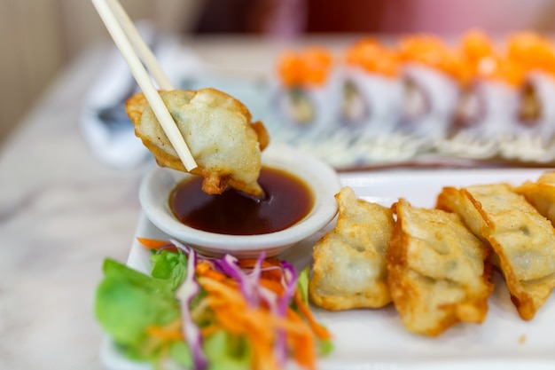 Schließen Sie herauf die Essstäbchen, die die Mehlklöße (japanisches Gyoza) festklemmen, die auf einem rustikalen Holztisch im chinesischen Restaurant sitzen.