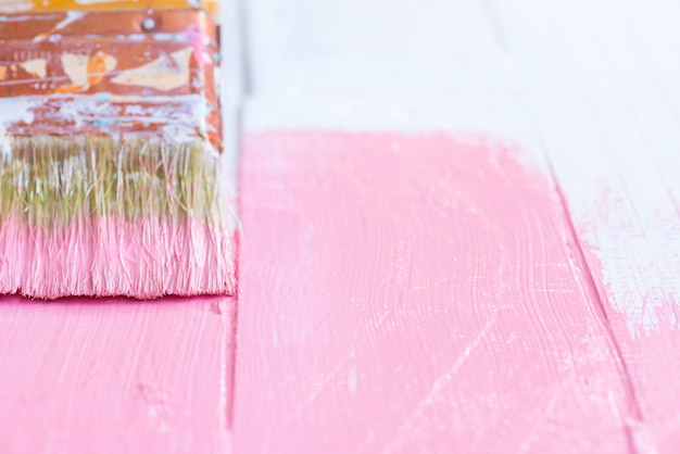 Schließen Sie herauf die Frauenhand, die Bürste hält, die rosa Farbe auf einem weißen Holztisch malt.