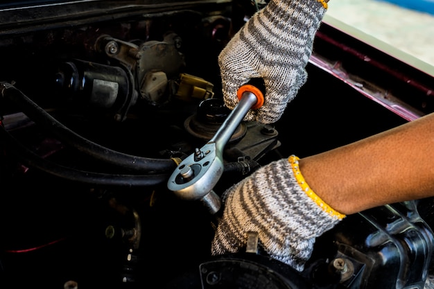 Schließen Sie herauf die Hand, die Automechaniker unter Verwendung eines Schlüssels und eines Schraubenziehers zum Arbeitsdienstauto in der Garage hält.