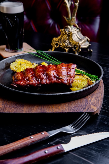 Schließen Sie herauf feinschmeckerisches Hauptgericht mit gegrilltem Schweinefleisch Rib und Fried Potatoes auf schwarzer Wanne. Auf Holzbrett serviert