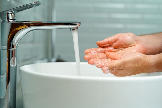 Schließen Sie herauf Foto der männlichen Hände, die mit Seife über dem Waschbecken drinnen waschen