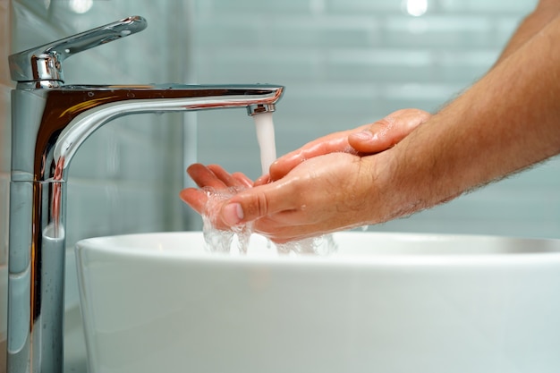 Schließen Sie herauf Foto der männlichen Hände, die mit Seife über dem Waschbecken drinnen waschen