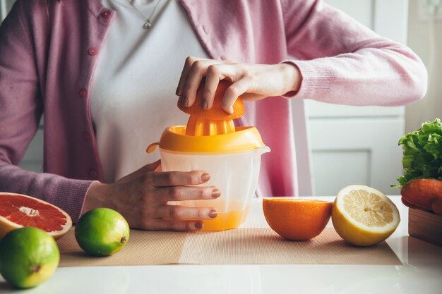 Schließen Sie herauf Foto einer Frau, die Saft zu Hause aus Früchten unter Verwendung eines manuellen Quetschers macht