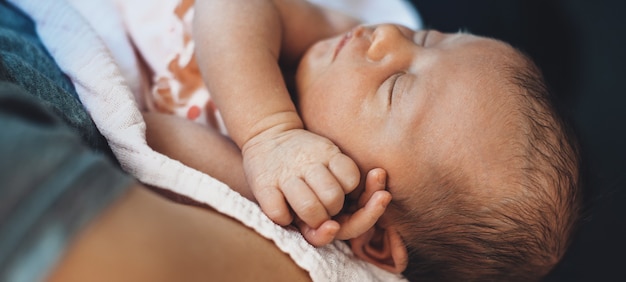 Schließen Sie herauf Foto von einem kaukasischen Neugeborenen, das schläft, während ihre Mutter sie hält und umarmt