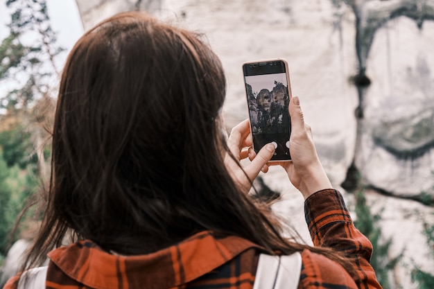 Schließen Sie herauf Frau in einem roten Hemd, das ein Foto oder ein Video des Felsens und des Waldes unter Verwendung ihres Smartphones macht