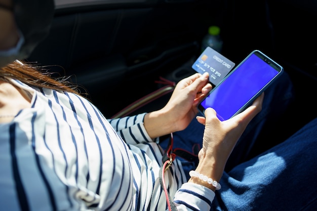 Schließen Sie herauf Frauenhände, die Smartphone und Kreditkarte halten, während Sie auf dem Rücksitz des Autos sitzen.