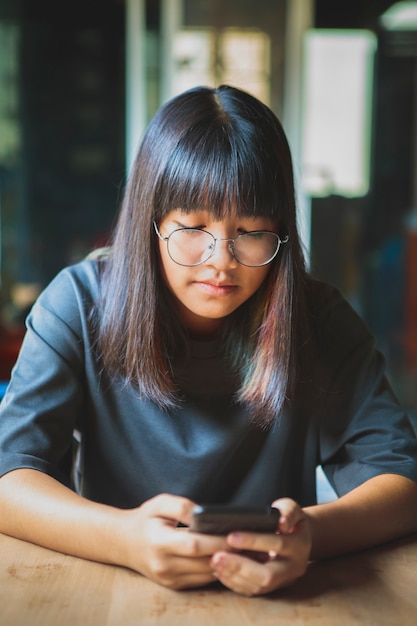 Schließen Sie herauf Gesicht des lächelnden Gesichtes des asiatischen Teenagers, das Smartphone in der Hand hält