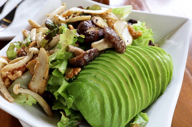 Foto schließen sie herauf gesunde mittagessenschüssel des strengen vegetariers. mit pilz, avocado, grüner eiche, roter eiche und pekannüssen, mit gesunder soße auf holztisch. lebensmittel