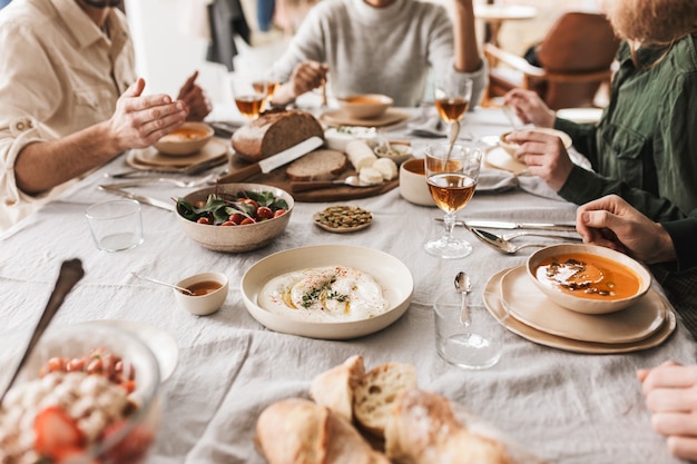 Schließen Sie herauf Gruppe der jungen Leute, die am Tisch voll des köstlichen Essens und der Gläser Wein sitzen, die im gemütlichen Café zu Mittag essen