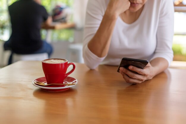 Schließen Sie herauf Hände der schönen jungen Frau, die Handy, Smartphone sitzt im Café hält. Weicher Fokus.