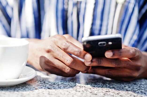 Schließen Sie herauf Hände des afrikanischen Mannes mit Handy und Tasse Kaffee