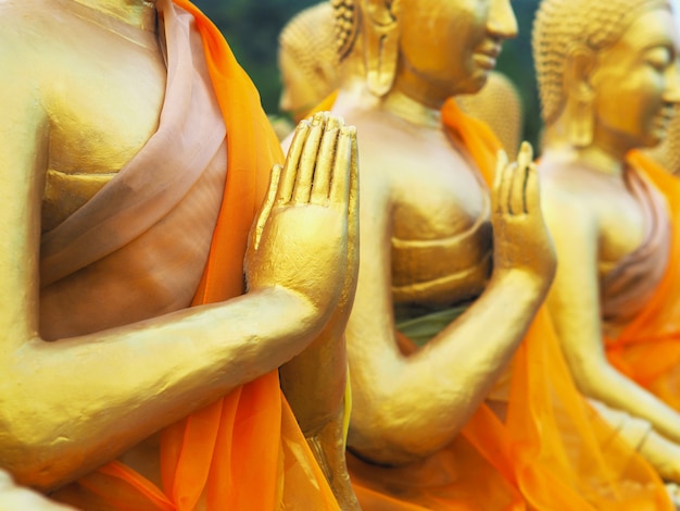 Schließen sie herauf hand der goldenen mönchstatuen, die in einer reihe am öffentlichen tempel nakornnayok provinz, thailand sitzen