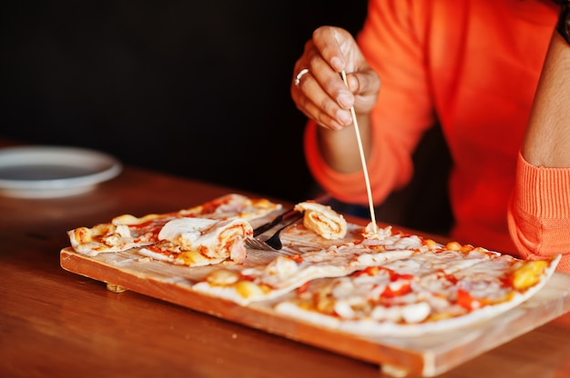 Schließen Sie herauf Hand des Mannes im orangefarbenen Pullover, der an der Pizzeria mit Pizza sitzt.