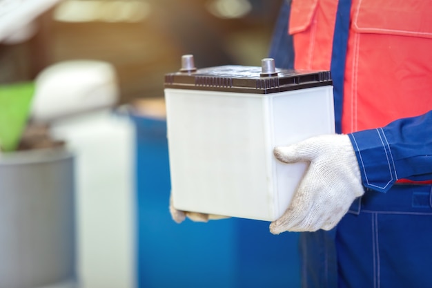 Schließen Sie herauf Hand-Techniker oder Automechaniker, der die Autobatterie im Autoreparatur-Autowerkstattzentrum hält.