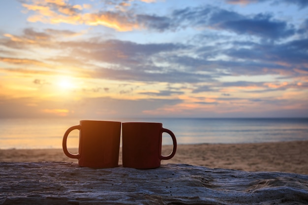 Schließen Sie herauf Kaffeetasse auf hölzernem Klotz am Sonnenuntergang- oder Sonnenaufgangstrand