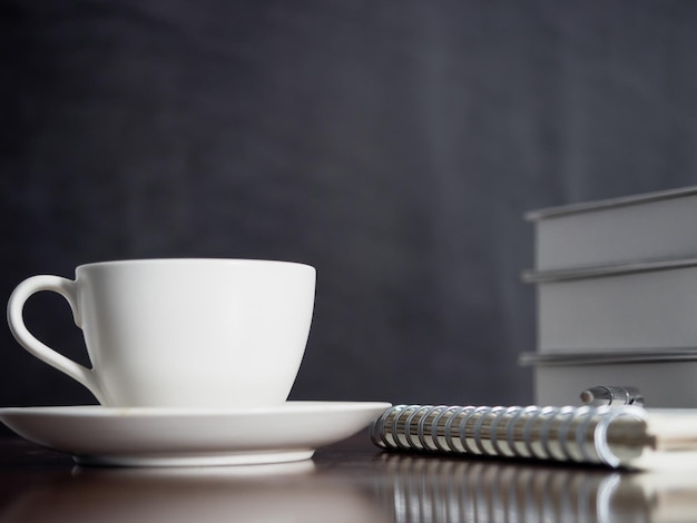 Schließen sie herauf kaffeetasse mit notizbuch und stift auf dunklem hintergrund des holztisches