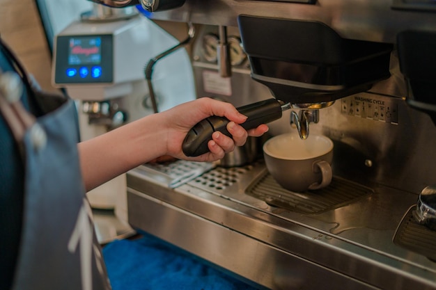 Schließen Sie herauf Mädchenhand, die einen Siebträger mit Morgenkaffee hält Kellner, der Latte macht