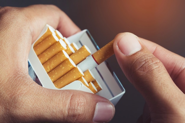 Schließen Sie herauf Mannhand, die schält es von der Zigarettenschachtel ab, bereiten das Rauchen einer Zigarette vor. Packaufstellung.